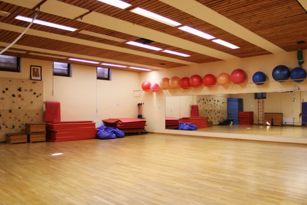 Gymnastikraum der Kurse mit Spiegelwand, Turnmatten und einer Reihe bunter Gymnastikbälle