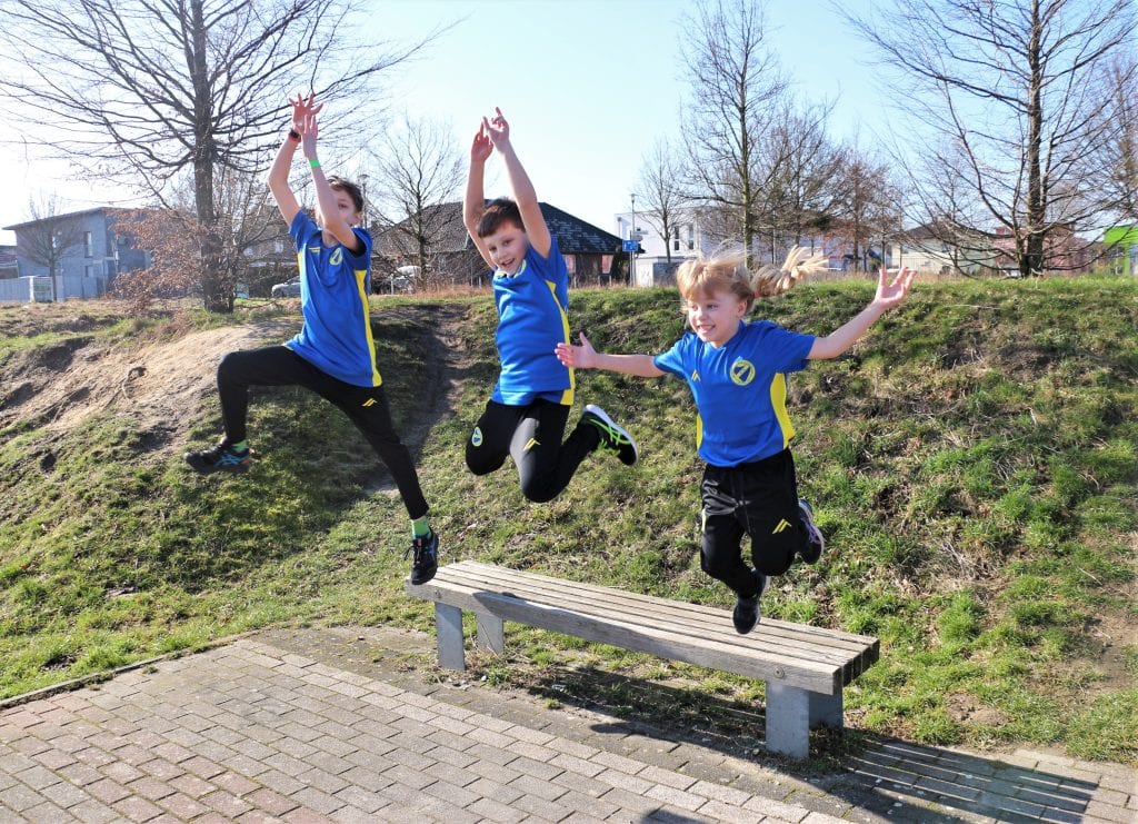 Drei Kinder in SFK-Trainingskleidung springen jubelnd über eine Bank